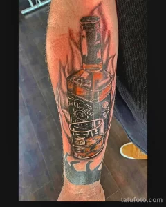 Фото тату реалистичного изображения бутылки Jack Daniel's и стакана виски на руке, выполненного в ярких цветах и с высокой детализацией.