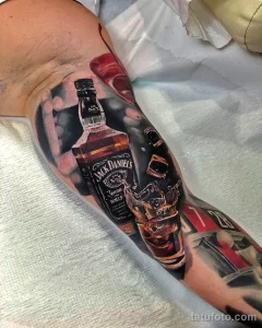 Фото тату реалистичного изображения бутылки Jack Daniel's и стакана виски на предплечье, выполненного в ярких цветах и с высокой детализацией.