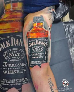 Фото тату на плече: масштабное изображение бутылки Jack Daniel's и этикетки. Реалистичный, детализированный рисунок татуировки.