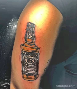Фото тату бутылки Jack Daniel's на руке. Рисунок выполнен в ярких цветах с использованием черного контура.
