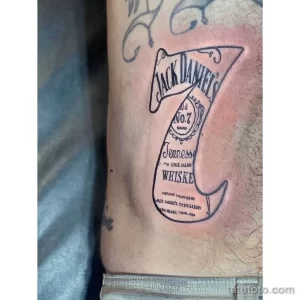 Фото тату черно-белой бутылки виски Jack Daniel's. Классический рисунок татуировки в стиле графика.