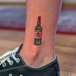 Фото тату маленькой бутылки виски Jameson на лодыжке. Лаконичный и стильный рисунок татуировки.