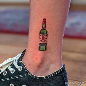 Фото тату маленькой бутылки виски Jameson на лодыжке. Лаконичный и стильный рисунок татуировки.