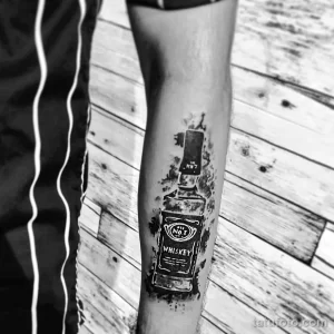 Фото тату Jack Daniel's на икре. Черно-белый рисунок бутылки виски с этикеткой, выполненный в технике акварели и с эффектом размытия.