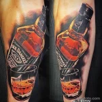Фото реалистичной татуировки на руке: бутылка Jack Daniel's и наполненный стакан виски. Детализированный рисунок татуировки с яркими цветами и тенями.