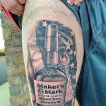 Фото крупной татуировки на ноге с изображением этикетки Maker's Mark, координат и декоративных элементов, выполненное в реалистичном стиле.