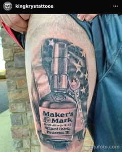 Фото крупной татуировки на ноге с изображением этикетки Maker's Mark, координат и декоративных элементов, выполненное в реалистичном стиле.