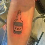Фото тату на руке с минималистичным изображением бутылки XXX, выполненной в черном цвете.