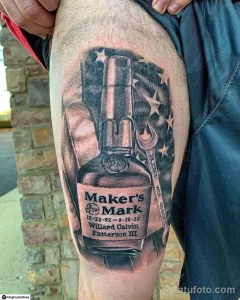 Фото тату на руке с изображением бутылки виски Maker's Mark, окруженной звездами и американским флагом.