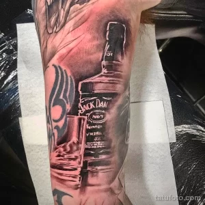 Детализированная татуировка на руке, изображающая бутылку виски Jack Daniel's с этикеткой и элементами декора.