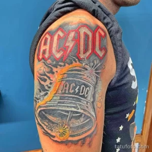Фото тату с логотипом группы AC/DC на плече. Яркий рисунок с использованием красного, серого и черного цветов.
