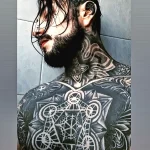 Фотография мужчины с масштабной татуировкой в геометрическом стиле, покрывающей его грудь, шею и плечи.