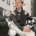 Фотография девушки с множеством татуировок на лице, шее и руках, а также с пирсингом, демонстрирующей свой альтернативный стиль.