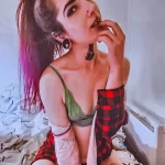Фотография девушки с татуировками на плече и руке, ярким макияжем и разноцветными волосами, демонстрирующая свой стиль.