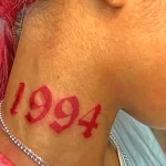 Фотография татуировки с годом рождения '1994' на шее девушки. Татуировка выполнена в красном цвете в стиле олдскул.