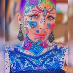 Фото тату на лице, шее и груди девушки, покрытых яркими, красочными рисунками в стиле психоделики и абстракции. Много цветов и деталей.