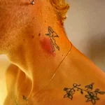 Фото тату с изображением феи и цветов на шее мужчины. Черно-белый рисунок, тонкие линии, минималистичный стиль. Нежный и загадочный дизайн.