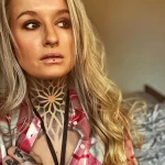 Фото тату с геометрическим узором на шее женщины. Черно-серый рисунок, точные линии, сложный дизайн. Современный и элегантный вид.