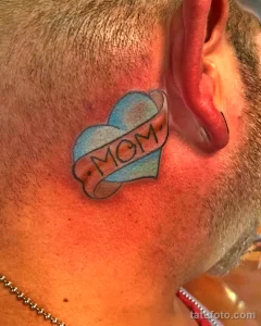 Фото тату: небольшая татуировка в виде сердца с надписью 'MOM' на шее. Классический и трогательный эскиз тату для выражения любви к матери.