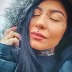 Фото молодой девушки с ярким макияжем и множеством татуировок на руках и шее. Видны рисунки в стиле олдскул и графика.