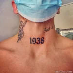 Фото тату: небольшая татуировка ангела и даты '1938' на затылке мужчины. Выполнена в традиционном стиле с использованием черных линий.