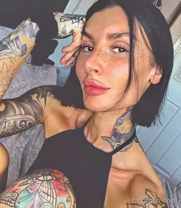 Фото тату: девушка с полным рукавом татуировок, демонстрирующая яркие и красочные рисунки на руке и шее.