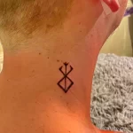 Фото тату с изображением символа 'Brand of Sacrifice' из манги 'Berserk' на шее мужчины. Татуировка выполнена в черном цвете.