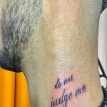 Фото тату: надпись "Do not judge me" на боку, выполненная каллиграфическим шрифтом в синем цвете.