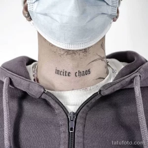 Фото тату: надпись "incite chaos" на шее мужчины. Черно-белый рисунок, готический шрифт, минималистичный стиль.