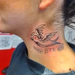 Фото тату с изображением летящей ласточки и надписи 'BTR' на затылке. Черно-серый рисунок в стиле традиционной татуировки. Эскиз татуировки с символическим значением.