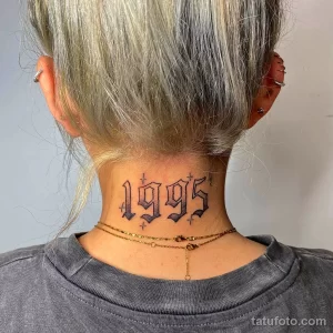 Фото тату с цифрами 1995 на затылке. Черный шрифт в стиле old school, небольшие крестики по бокам. Минималистичный рисунок татуировки.