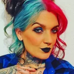 Фотография девушки с яркой татуировкой бабочек на шее и плече. Бабочки выполнены в синих и красных тонах, с детальной проработкой крыльев.