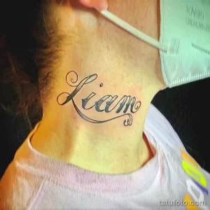 Фото татуировки с именем 'Liam', выполненной красивым каллиграфическим шрифтом на шее. Минималистичный рисунок татуировки.
