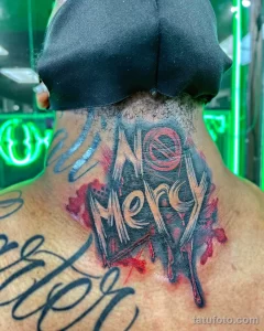 Фото тату с надписью 'No Mercy' на затылке, выполненное в ярких красных и черных тонах с брызгами краски. Динамичный рисунок татуировки.