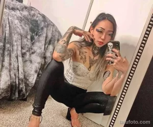 Фото татуировки в виде рукава на руке девушки с темными волосами. Изображены яркие цветы, череп и другие элементы в смешанном стиле.