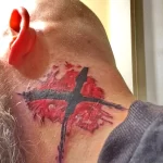 Фото татуировки птицы в стиле акварель на шее мужчины. Рисунок выполнен в ярких красных и черных тонах с использованием размытых красок.