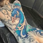 Красочная татуировка павлина с распущенным хвостом на плече и шее женщины. Детализированный и яркий рисунок татуировки.