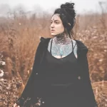 Фотография девушки с яркими и красочными татуировками на лице, шее и груди. Татуировки выполнены в стиле олдскул и акварель.
