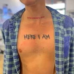 Фото тату: татуировка надписи "Everything's fine" и "HERE I AM" на груди мужчины. Рисунок выполнен красными чернилами в небрежном стиле.
