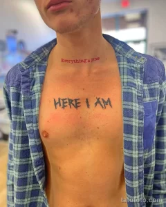 Фото тату: татуировка надписи "Everything's fine" и "HERE I AM" на груди мужчины. Рисунок выполнен красными чернилами в небрежном стиле.