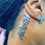 Фото тату: изящная надпись "Matériel", выполненная каллиграфическим шрифтом на шее девушки. Минималистичный рисунок татуировки.