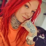 Фотография девушки с рыжими волосами, демонстрирующая татуированный рукав на руке и шее. На татуировке изображена сложная мандала и реалистичная роза.