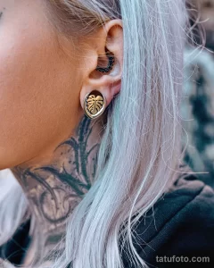 Фото минималистичной татуировки за ухом: изображение листьев монстеры, выполненное тонкими линиями. Изящный пример небольшой татуировки.