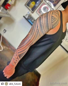 Фото тату: татуировка в стиле трайбл, покрывающая руку и плечо. Черные и коричневые узоры, геометрические формы и традиционные полинезийские мотивы.