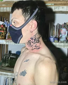Фото татуировки дракона на шее мужчины, выполненной в черном цвете в стиле графика. Виден фрагмент татуировки на плече.