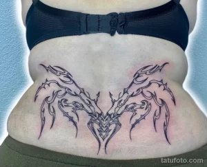 Фото тату: черная татуировка крыльев на пояснице, выполненная в стиле blackwork с использованием плотных черных линий и геометрических узоров.