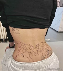 Фото тату: изящная татуировка в стиле line work на спине, изображающая цветы и растения. Черно-белый рисунок с тонкими линиями и детальной проработкой.