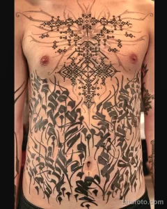 Фото тату на груди и животе: сложный узор в стиле dotwork, сочетающий геометрические фигуры и растительные элементы.