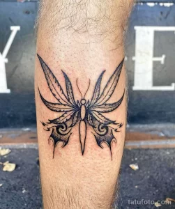 Фото татуировки бабочки, выполненной в стиле blackwork на голени. Изображение состоит из четких линий и геометрических форм, создающих силуэт бабочки.