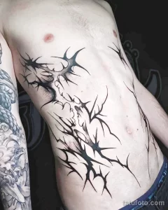 Фото тату: татуировка в стиле Blackwork на боку, изображающая абстрактное лицо, выполненное черными точками и линиями. Мрачный и загадочный дизайн.